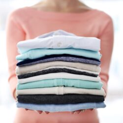 a women holding a stack of clothes that are folded
