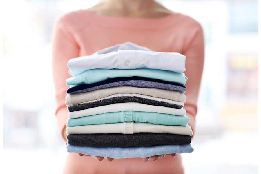 a women holding a stack of clothes that are folded